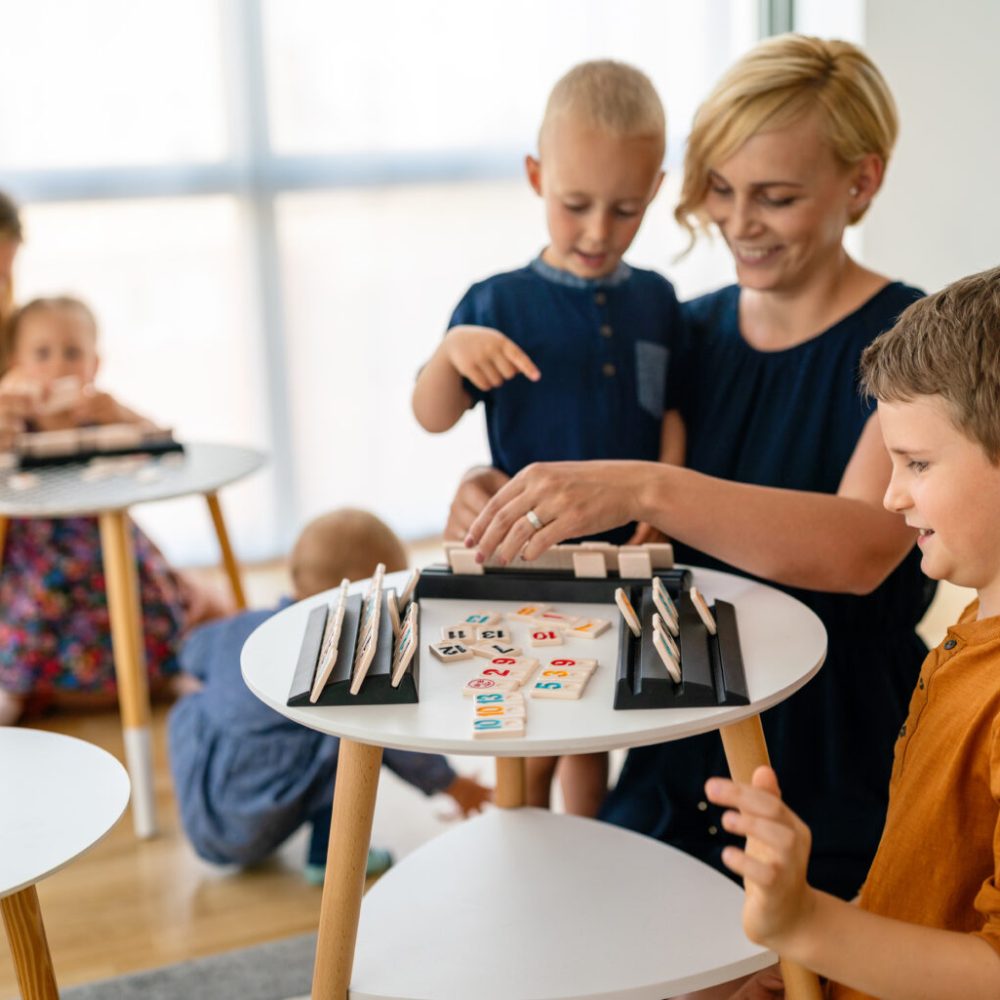 Young women at the table playing board game with children. Family, nursery, childhood concept.